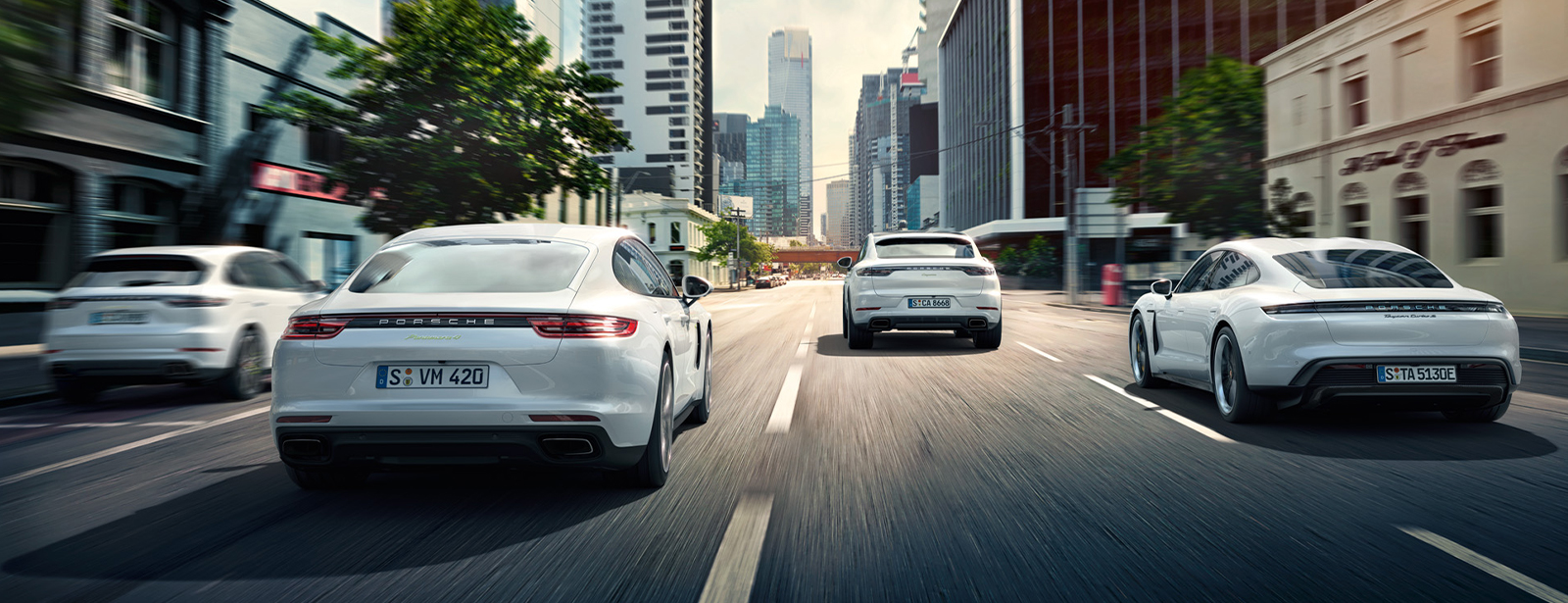 Vier Porsche E-Performance Fahrzeuge fahren vierspurig in einer Großstadt.